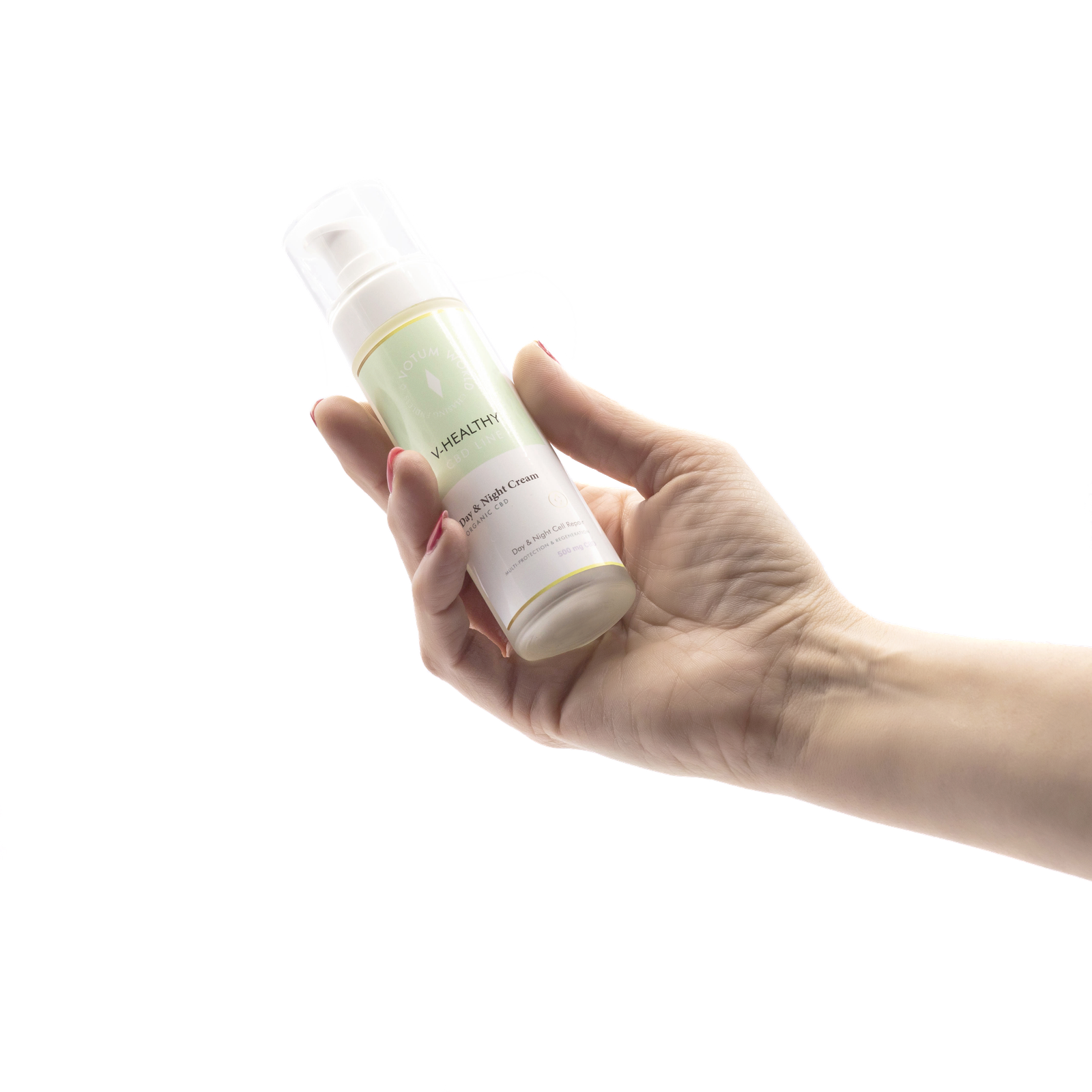 Mano femenina sosteniendo un envase de Day & Night Cream con etiqueta verde claro, mostrando el producto en posición inclinada sobre un fondo negro.